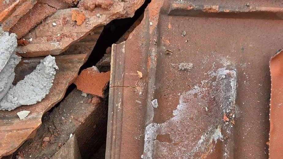 Broken terracotta tiles and old mortar exposing timber battens on a leaking roof in Essendon