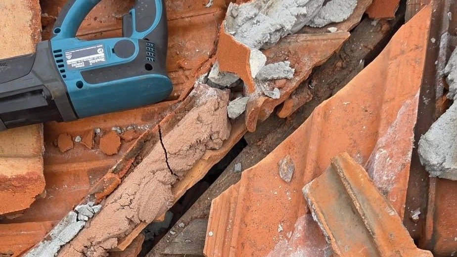 Cracked old mortar and broken terracotta tiles beside a rotary hammer during roof leak repairs in Essendon