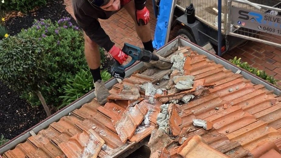 Roofer using a rotary hammer to remove old ridge bedding from a terracotta tiled roof in Essendon