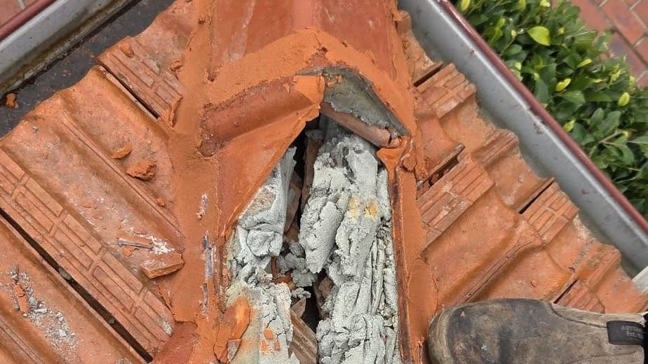 Cracked terracotta ridge tile with crumbling mortar bedding exposed on a roof in Essendon