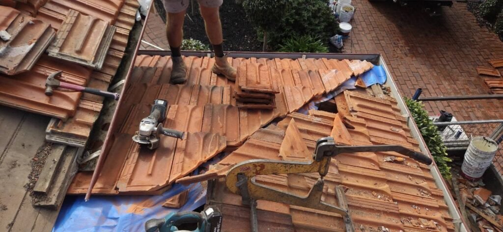 Roofer cutting terracotta tiles on a roof with new sarking laid during leak repairs in Essendon